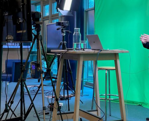  Furniture, Table, Desk, Adult, Male, Man, Person, Crowd, Clothing, Coat, Face, Head, Computer, Electronics, Laptop, Pc, Standing Desk
